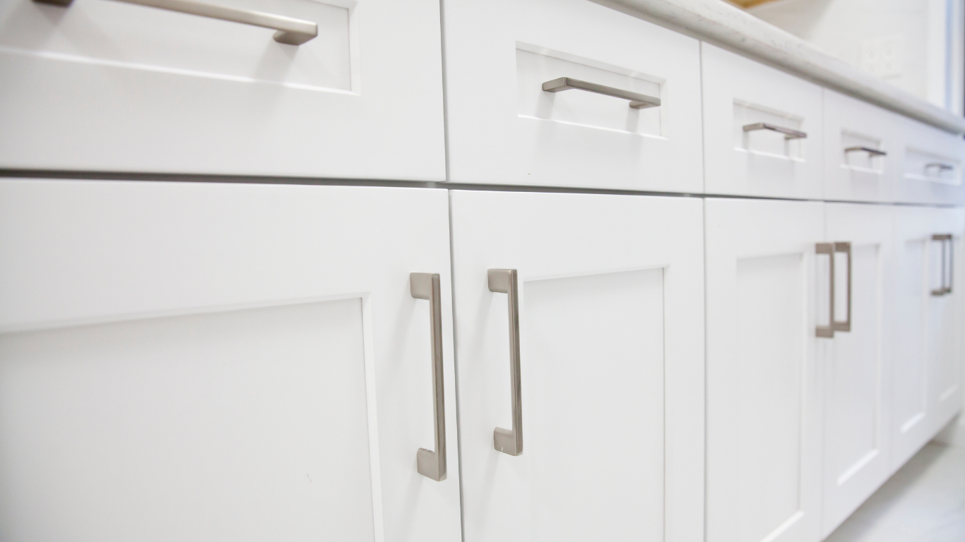 White kitchen cabinets with silver handles along a countertop.