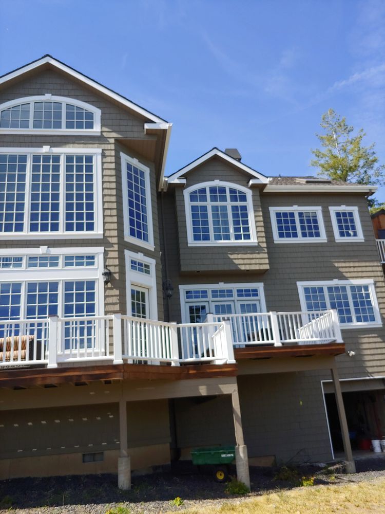 Large modern gray house with white trim, many windows, and a raised balcony under a blue sky