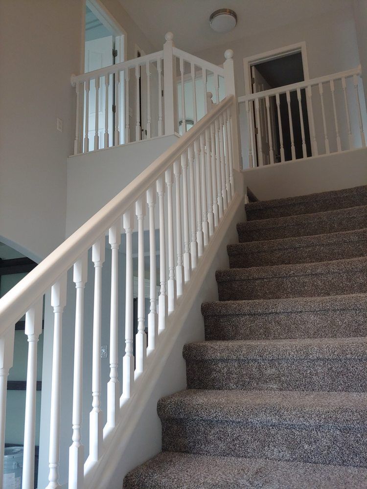 Indoor carpeted staircase with white railing leading to an upstairs landing