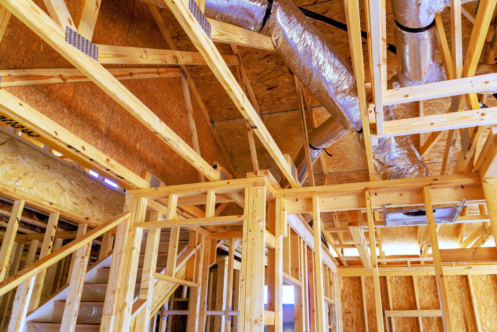 Wood-framed house interior under construction with exposed beams, studs, and insulation in the ceiling