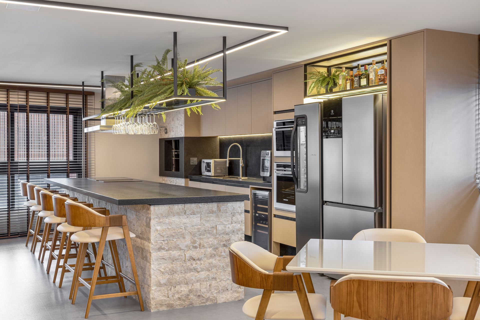 Cozinha moderna com ilha, balcão com banquetas, eletrodomésticos em aço inoxidável e vegetação suspensa.