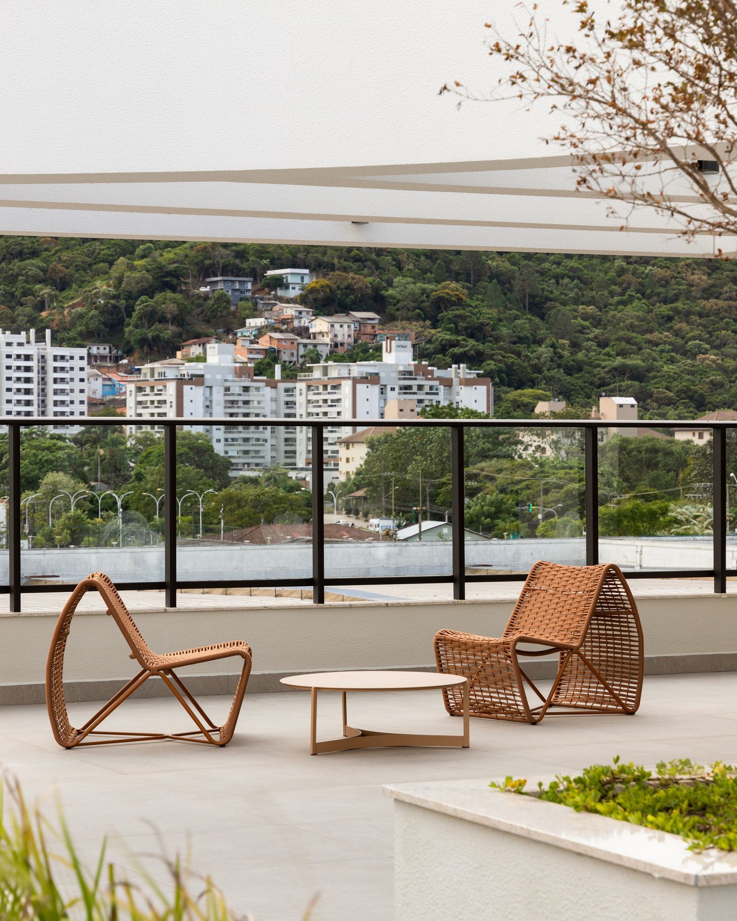 Terraço na cobertura com cadeiras e mesa de vime, com vista para a cidade e colinas verdejantes.