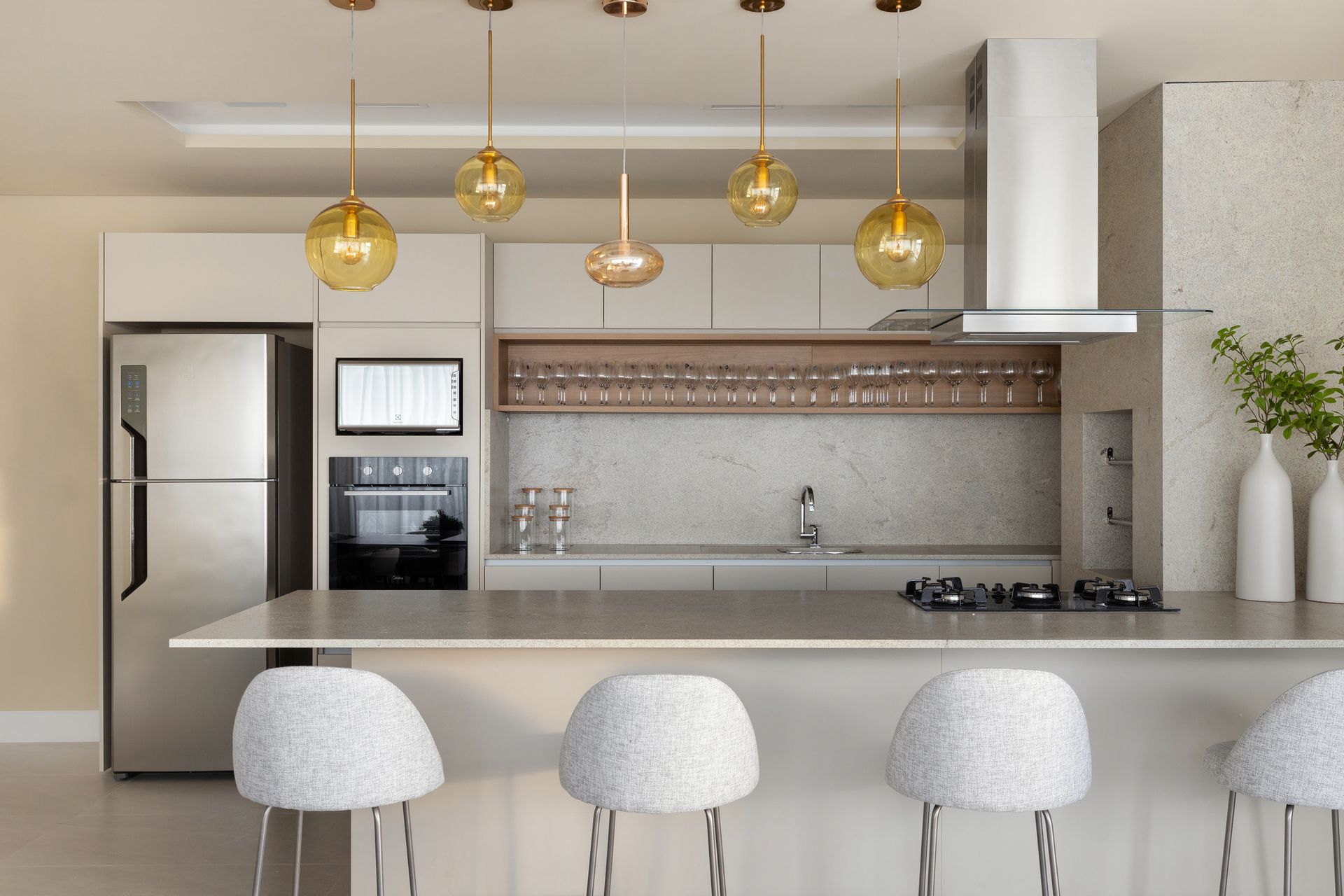 Cozinha moderna com armários brancos, eletrodomésticos de aço inoxidável e luminárias pendentes.