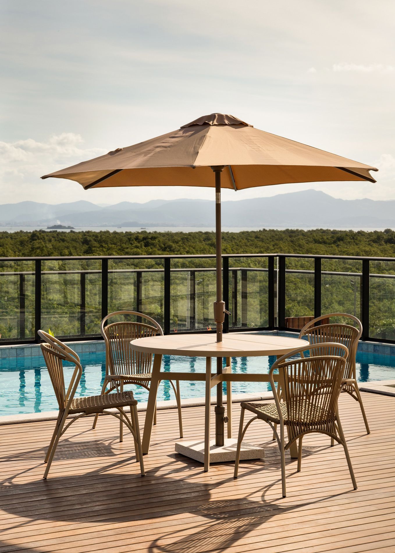 Mesa de jantar ao ar livre junto à piscina com vista para o mar, guarda-sol bege e cadeiras bege.