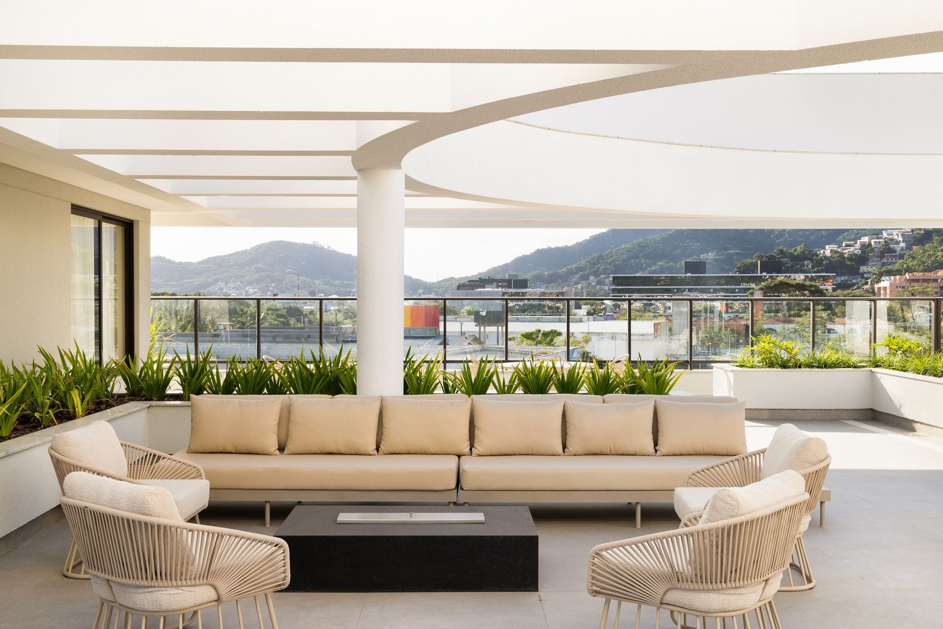 Lounge na cobertura com sofás bege, cadeiras de vime e lareira embutida com vista para a montanha.