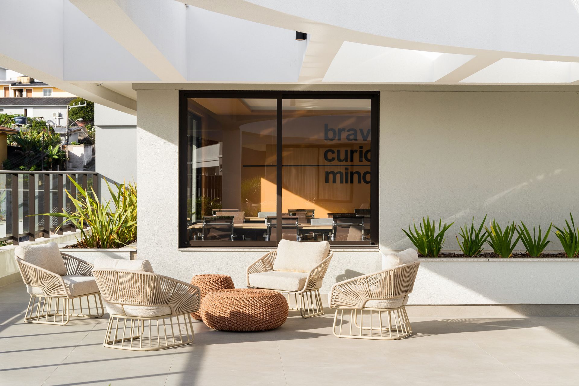 Pátio externo com cadeiras de vime, uma mesa baixa e uma janela com os dizeres 