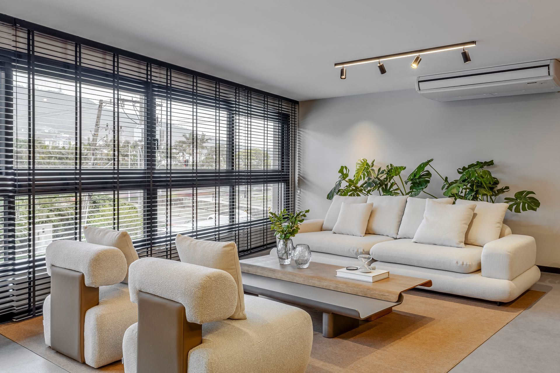 Sala de estar com sofá branco, duas poltronas e plantas junto à janela.