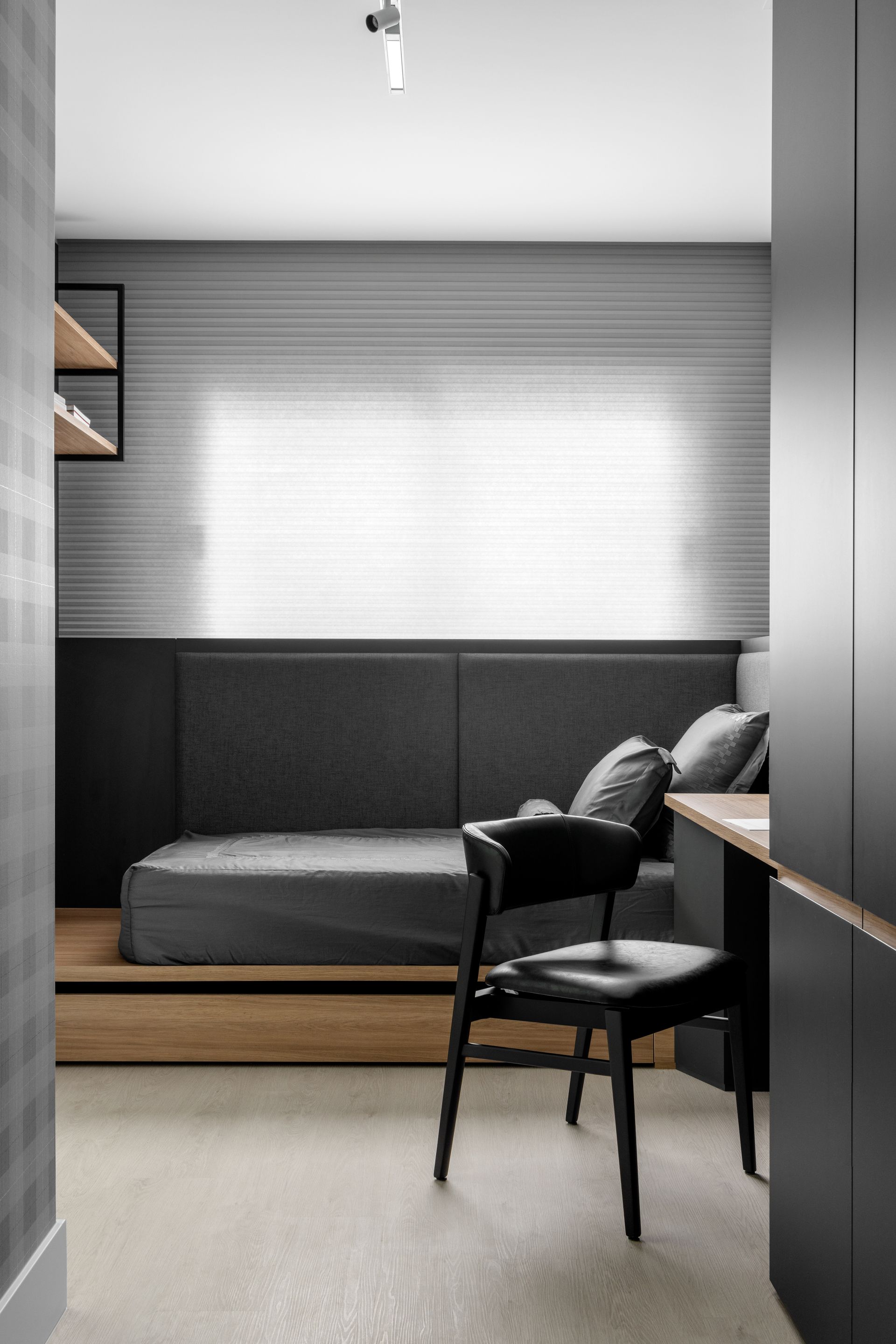 Quarto moderno com cama, escrivaninha, cadeira preta e detalhes em cinza e madeira.