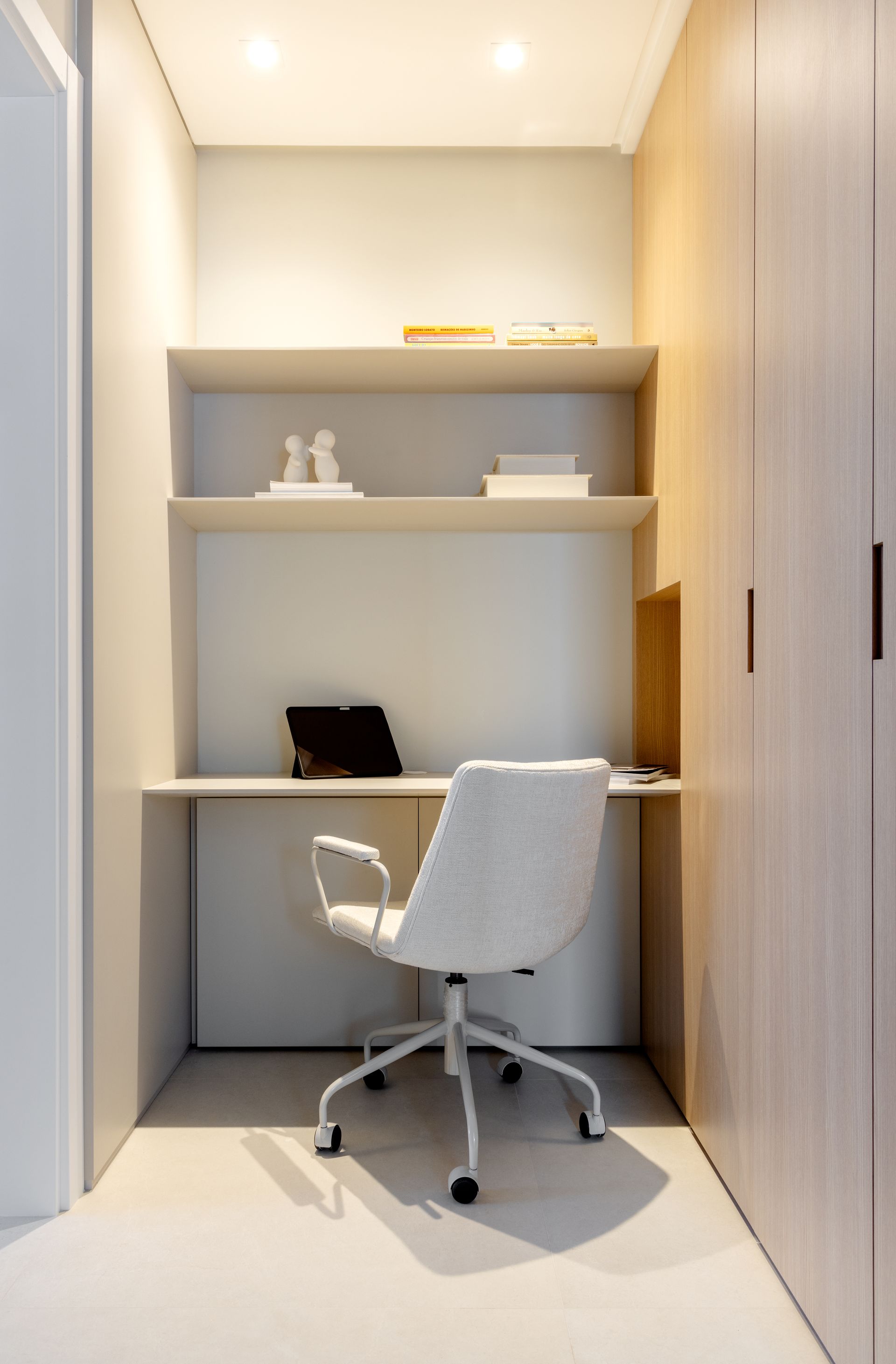 Pequeno escritório em casa com mesa, cadeira, prateleiras e armários de madeira.