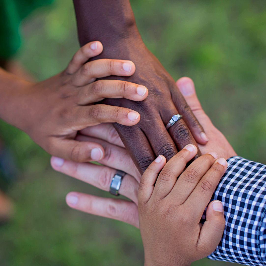 Hands stacked together outdoors, symbolizing teamwork and unity.