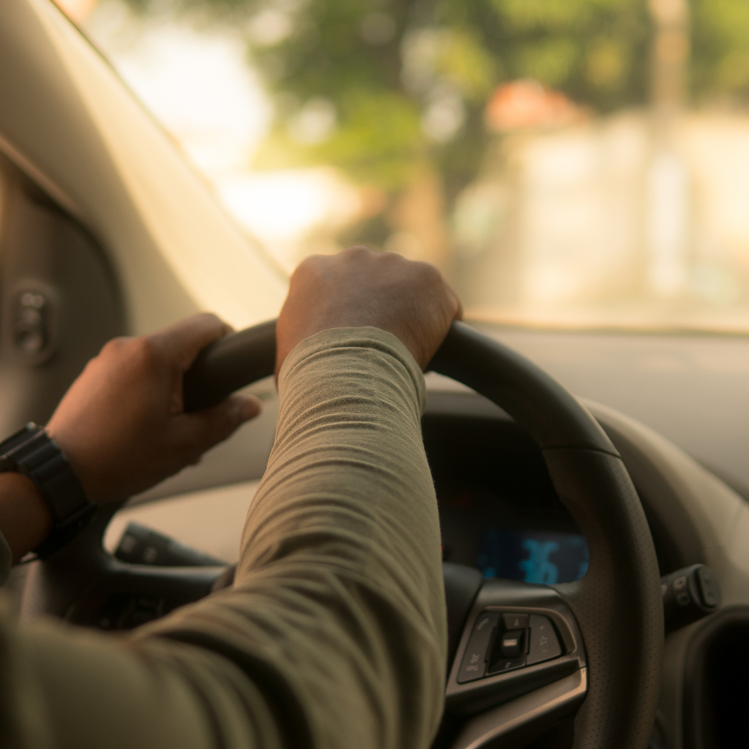 Hands on a car steering wheel while driving on a sunlit road