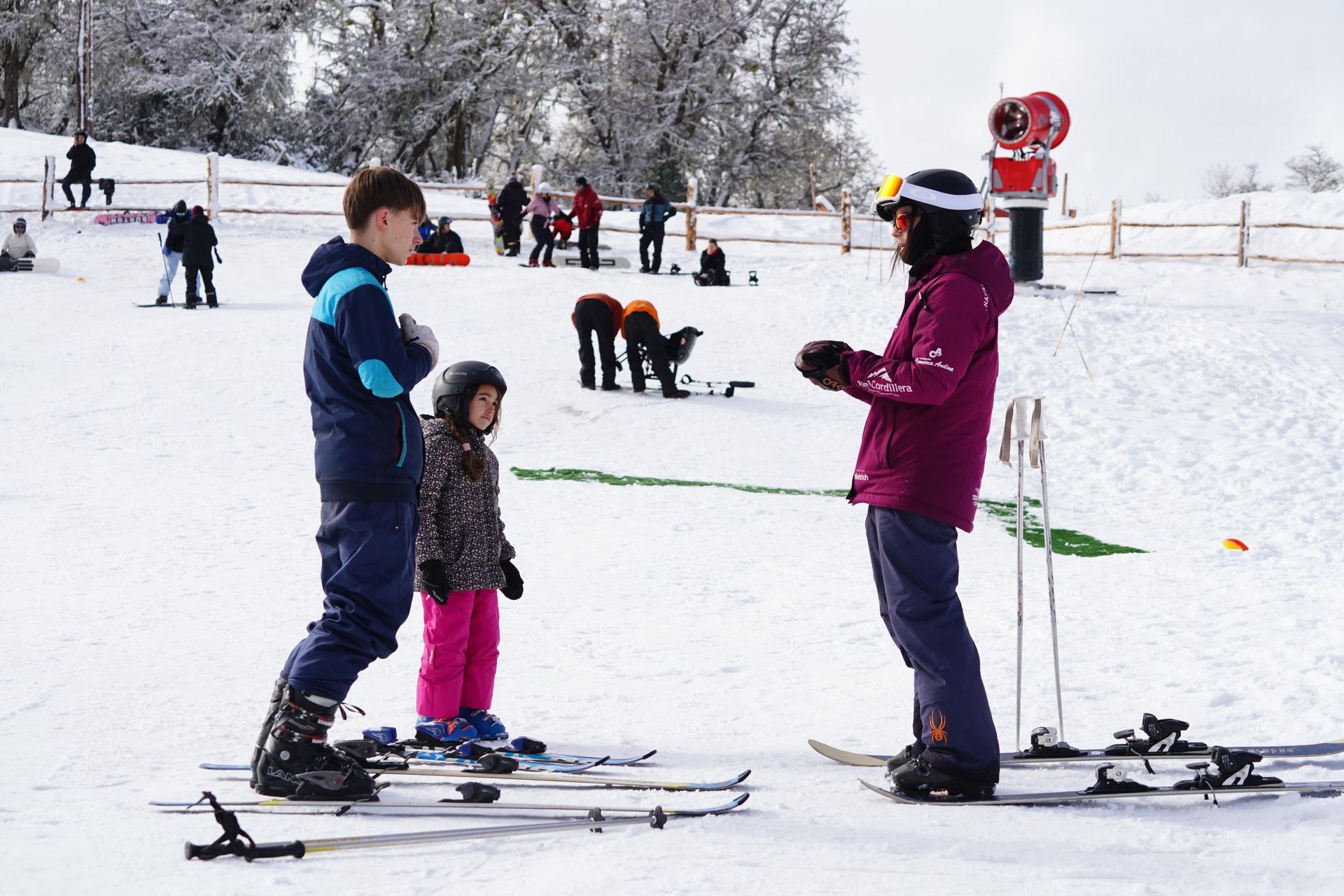Gente esquiando en una escuela de esquí nevada, con un instructor dando clase a dos niños al aire libre.