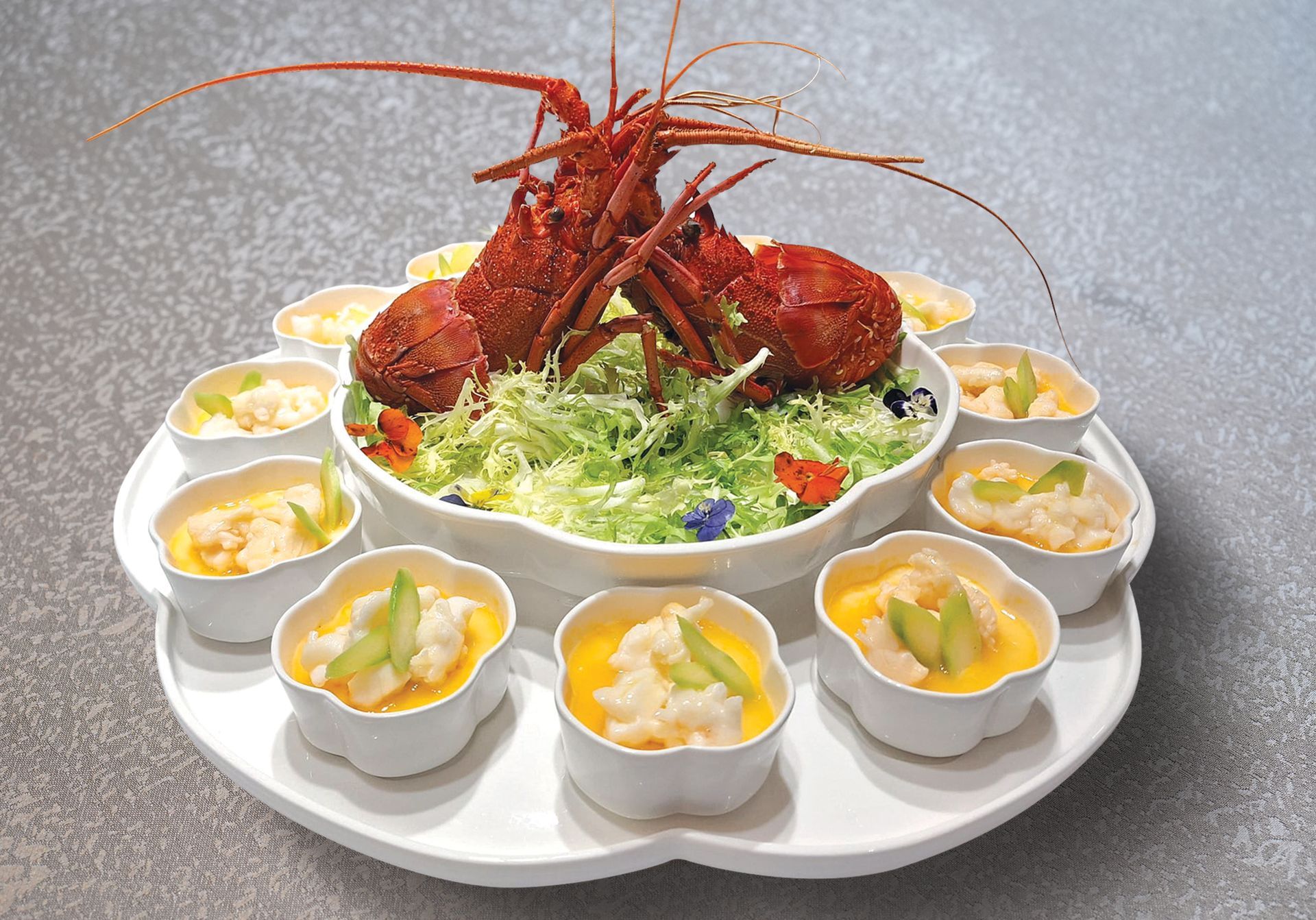Lobster and small side dishes on a tiered serving platter. Red lobster centerpiece, yellow and white side dishes.