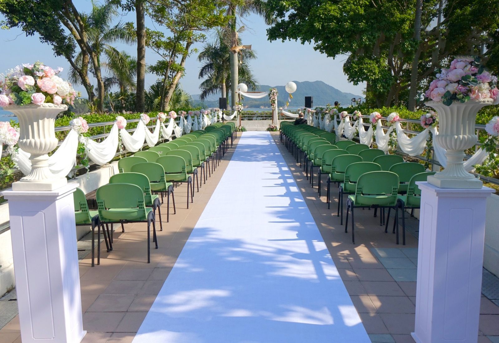Wedding ceremony setup with white aisle, green chairs, and floral decorations.
