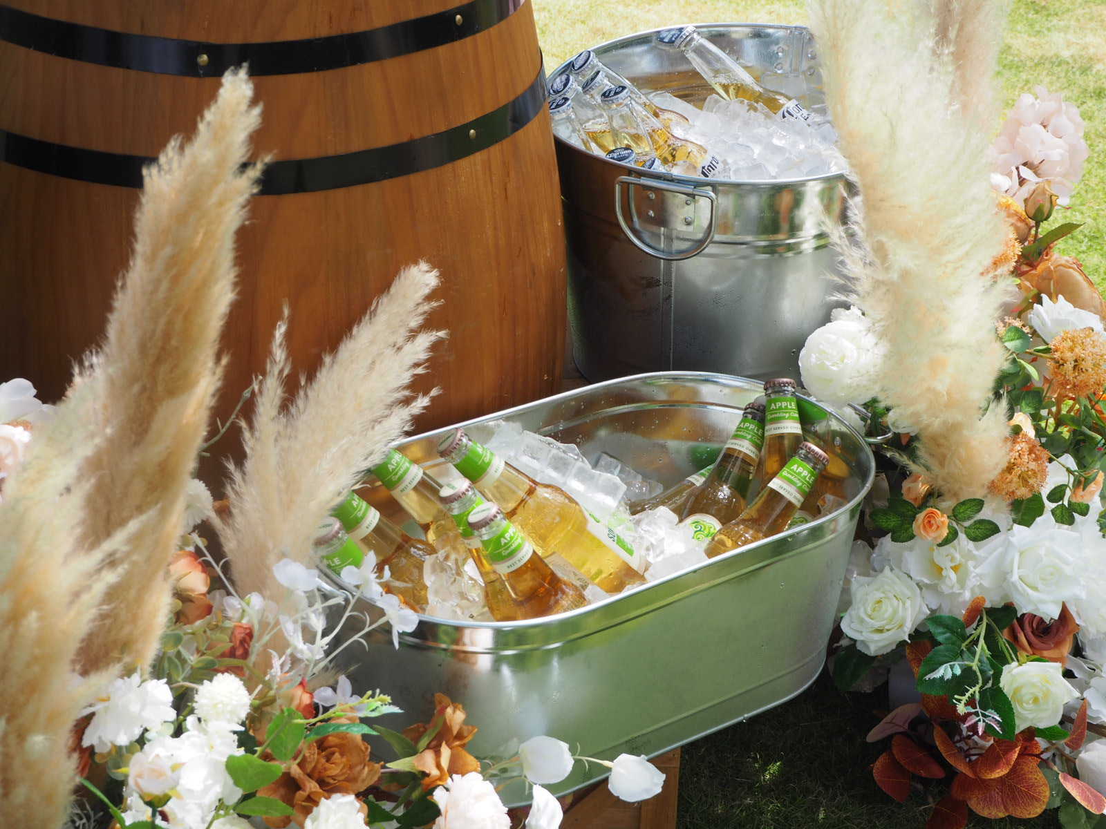 Beer in ice buckets, barrel, floral decor. Outdoor event setting.
