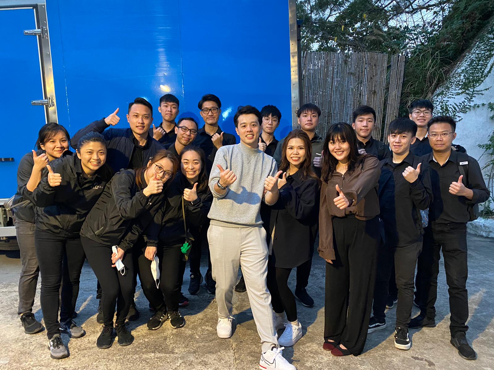 Group of people giving thumbs up pose near a large blue structure.
