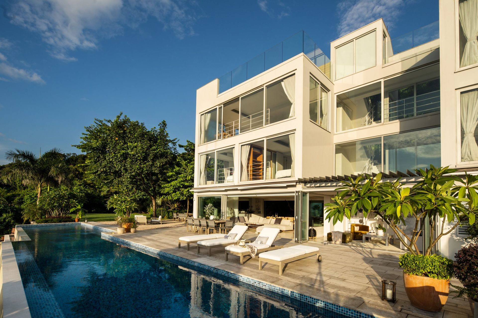 Modern white house with large windows, an infinity pool, and lounge chairs.