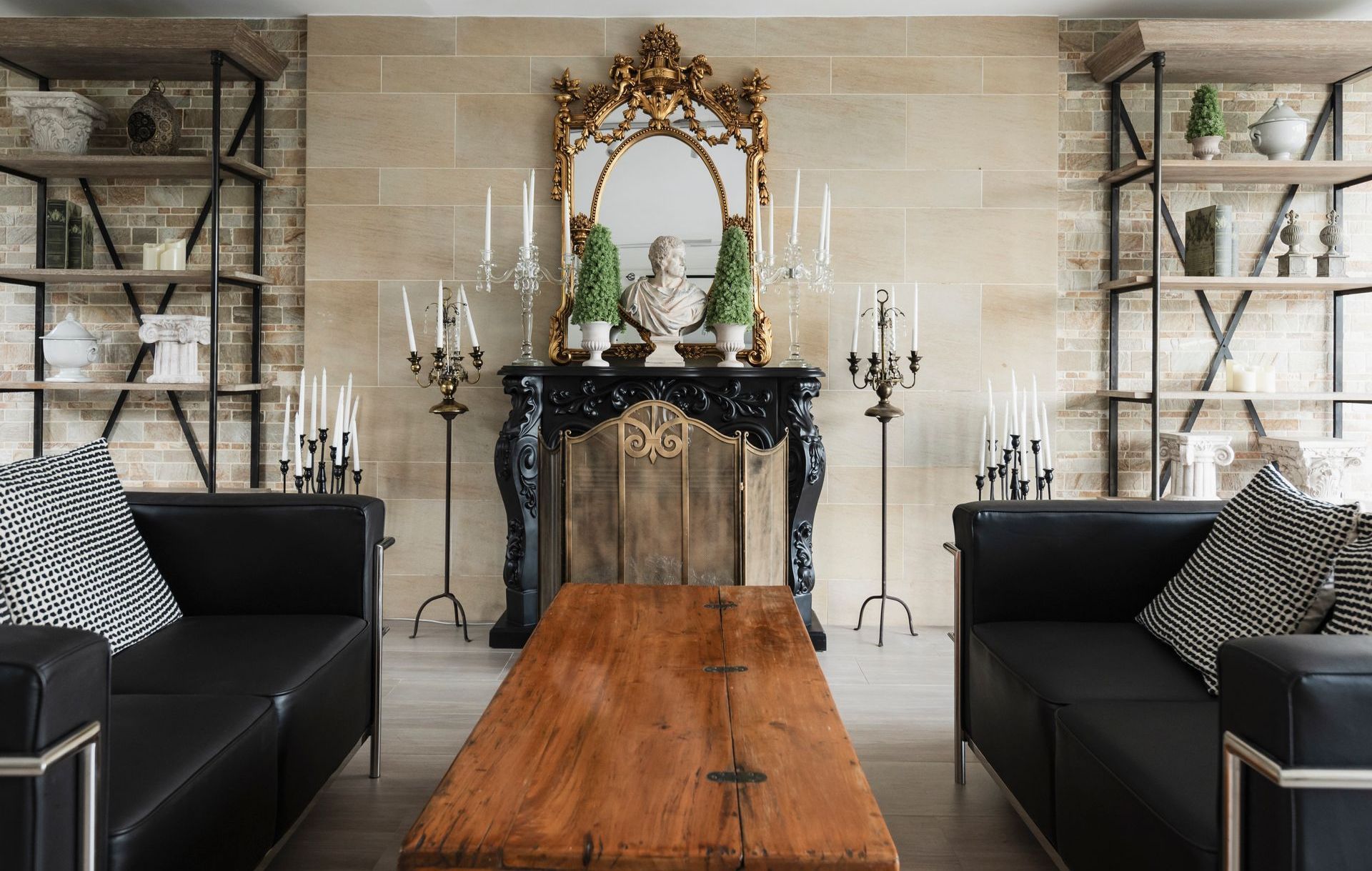 Living room with black sofas, wooden coffee table, ornate fireplace, and bookshelves.