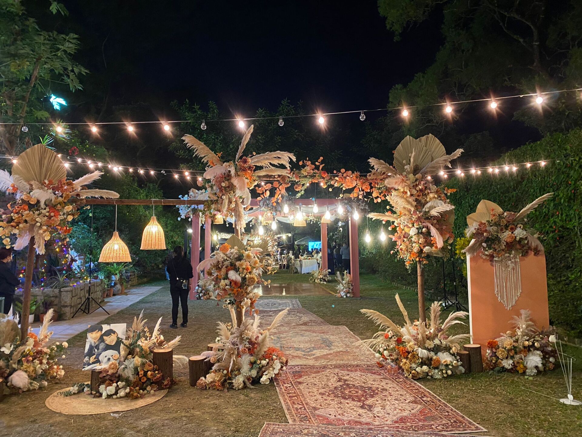 Wedding reception at night with floral archway, string lights, and rug leading to party.