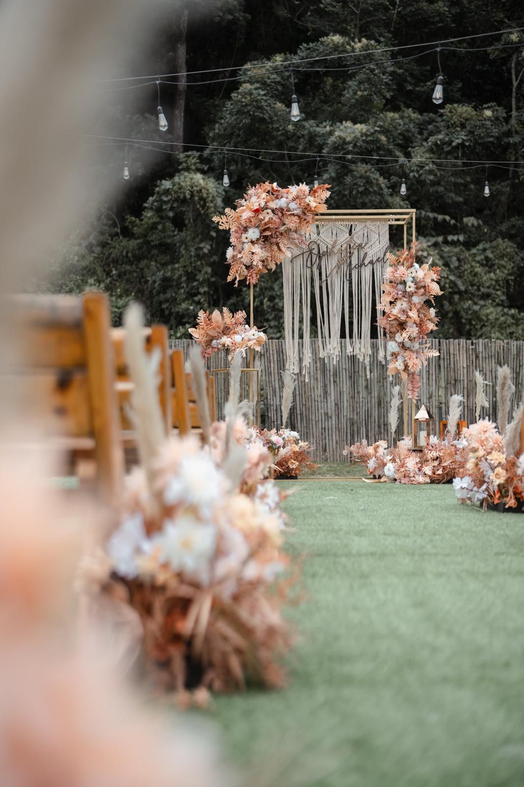 Outdoor wedding ceremony setup with floral arrangements and macrame backdrop.