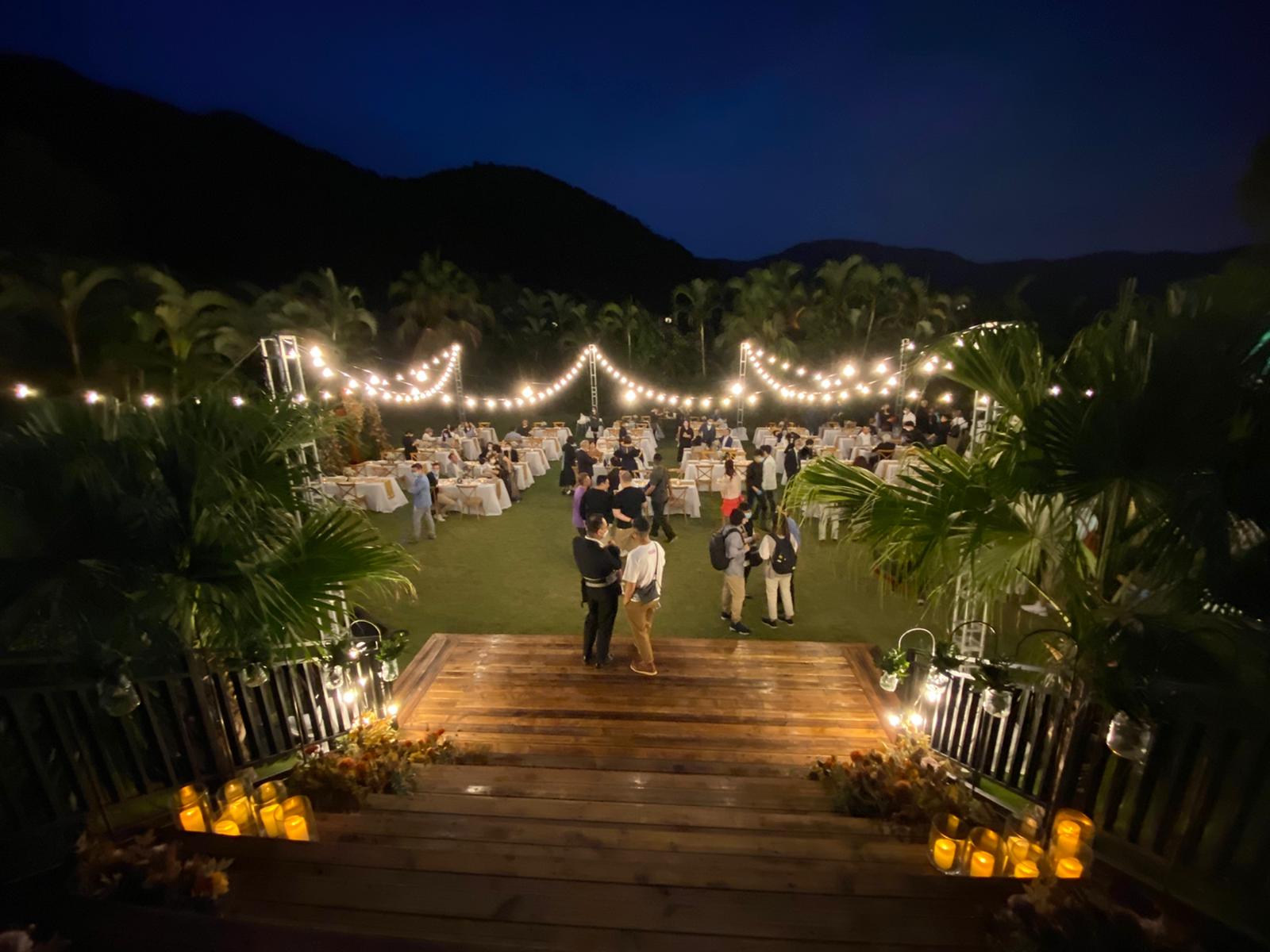 Outdoor wedding reception at night with string lights, tables, and mountain backdrop.