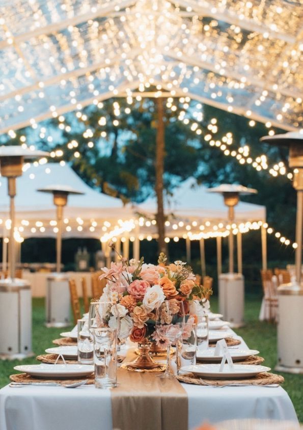 Wedding reception table set under a tent with string lights, floral centerpiece.