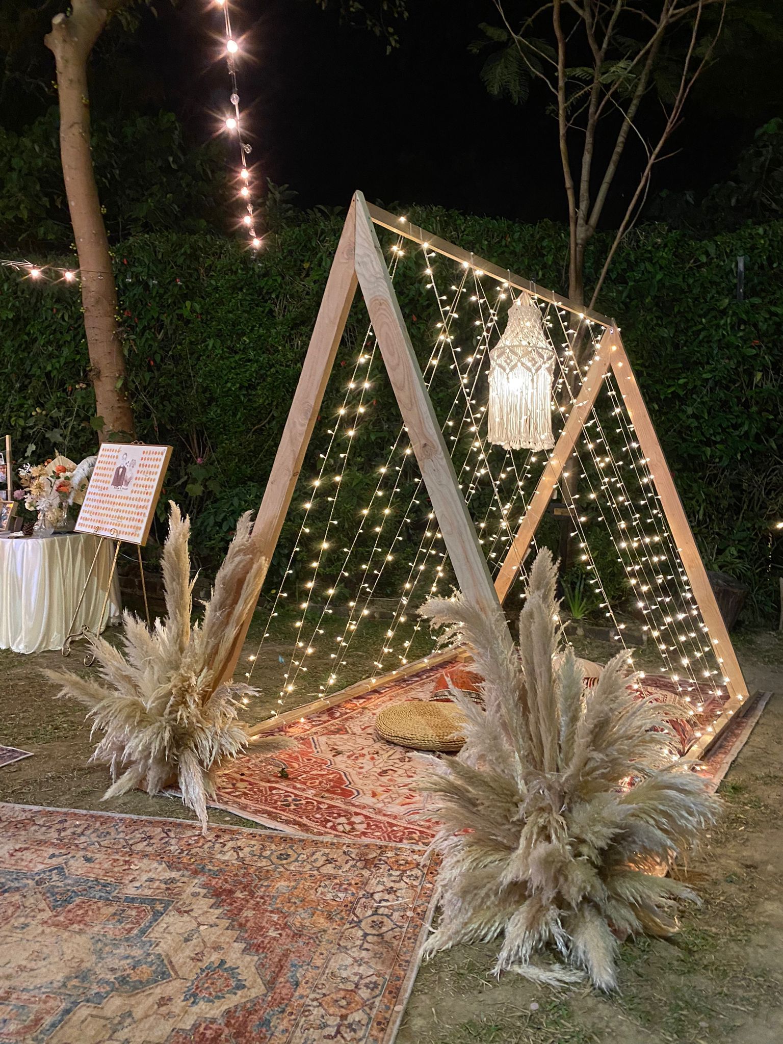 Wooden A-frame with string lights, rug, and pampas grass decorations, set outdoors at night.