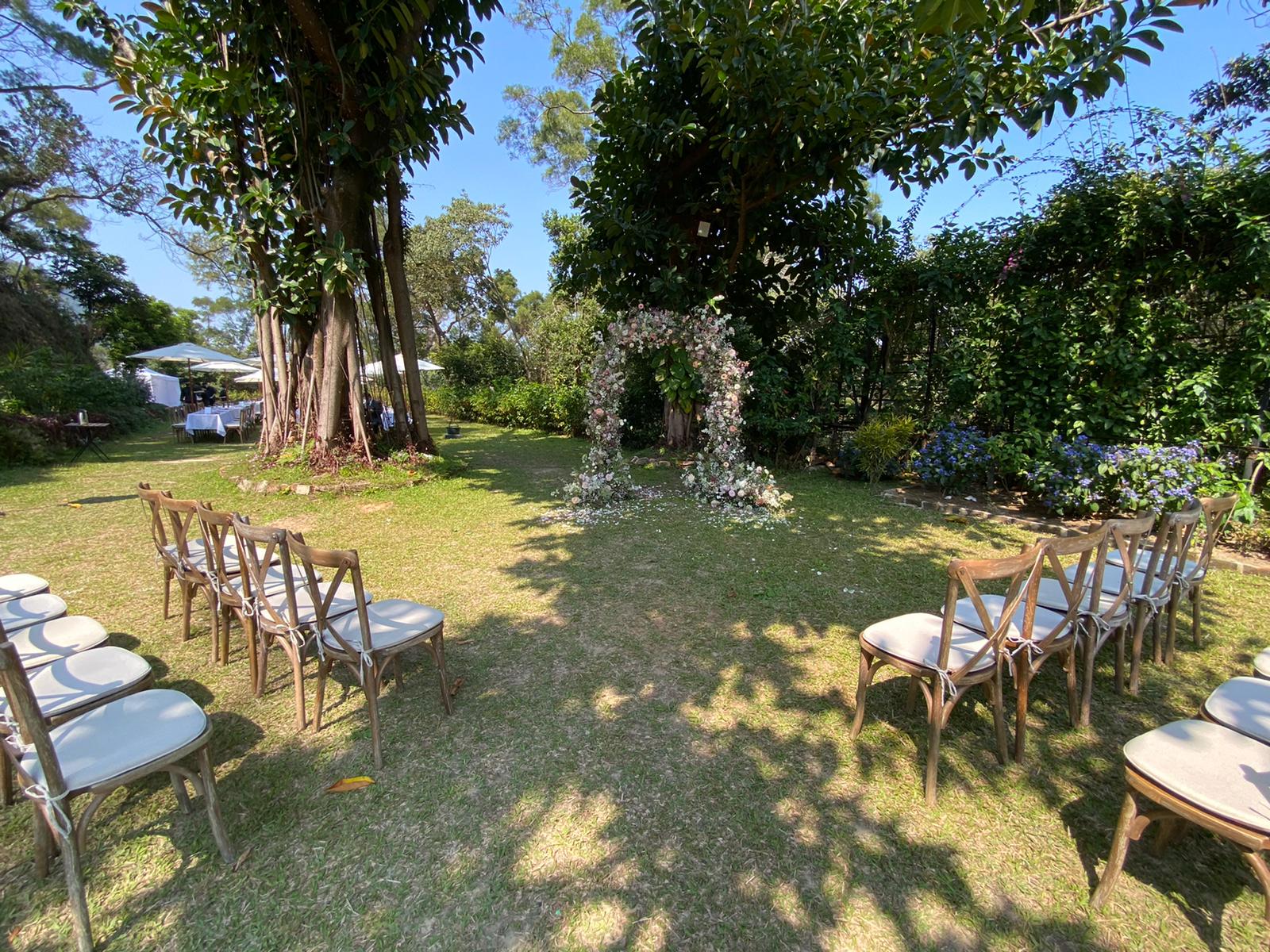 Wedding ceremony setup in a sunny garden with chairs facing a floral archway.