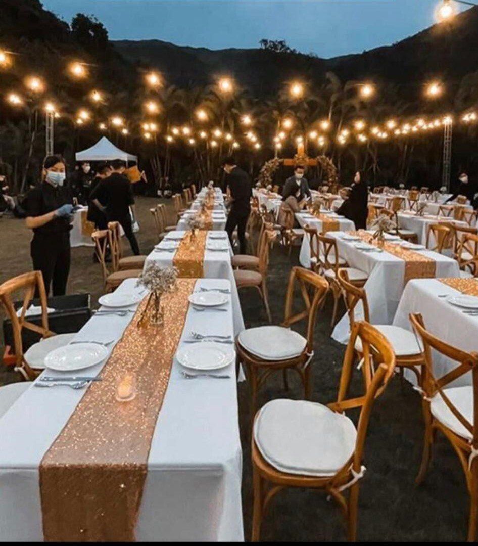 Outdoor event with tables set for a gathering, decorated with gold runners and string lights.