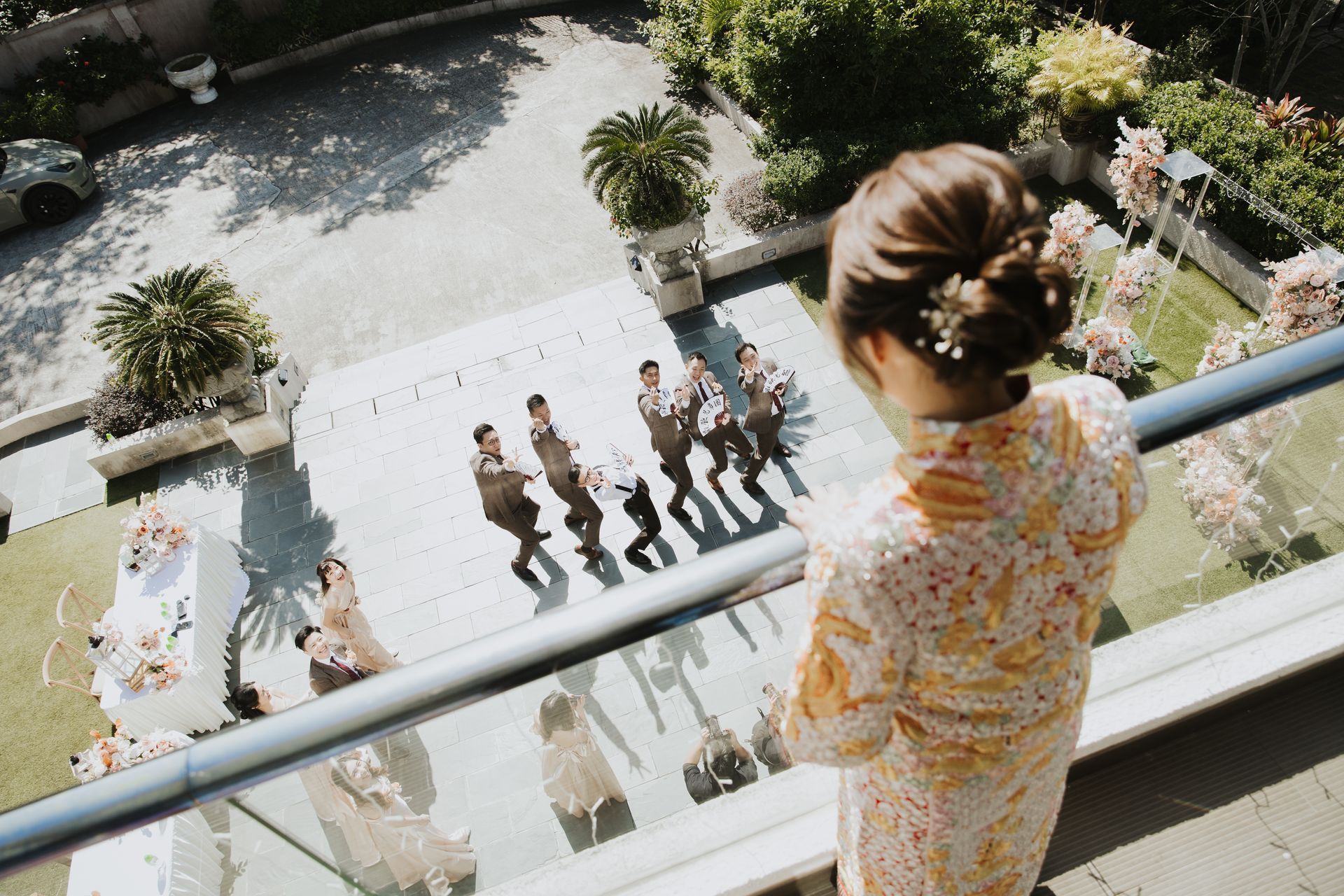 Woman watching wedding party dancing on a patio from a balcony.