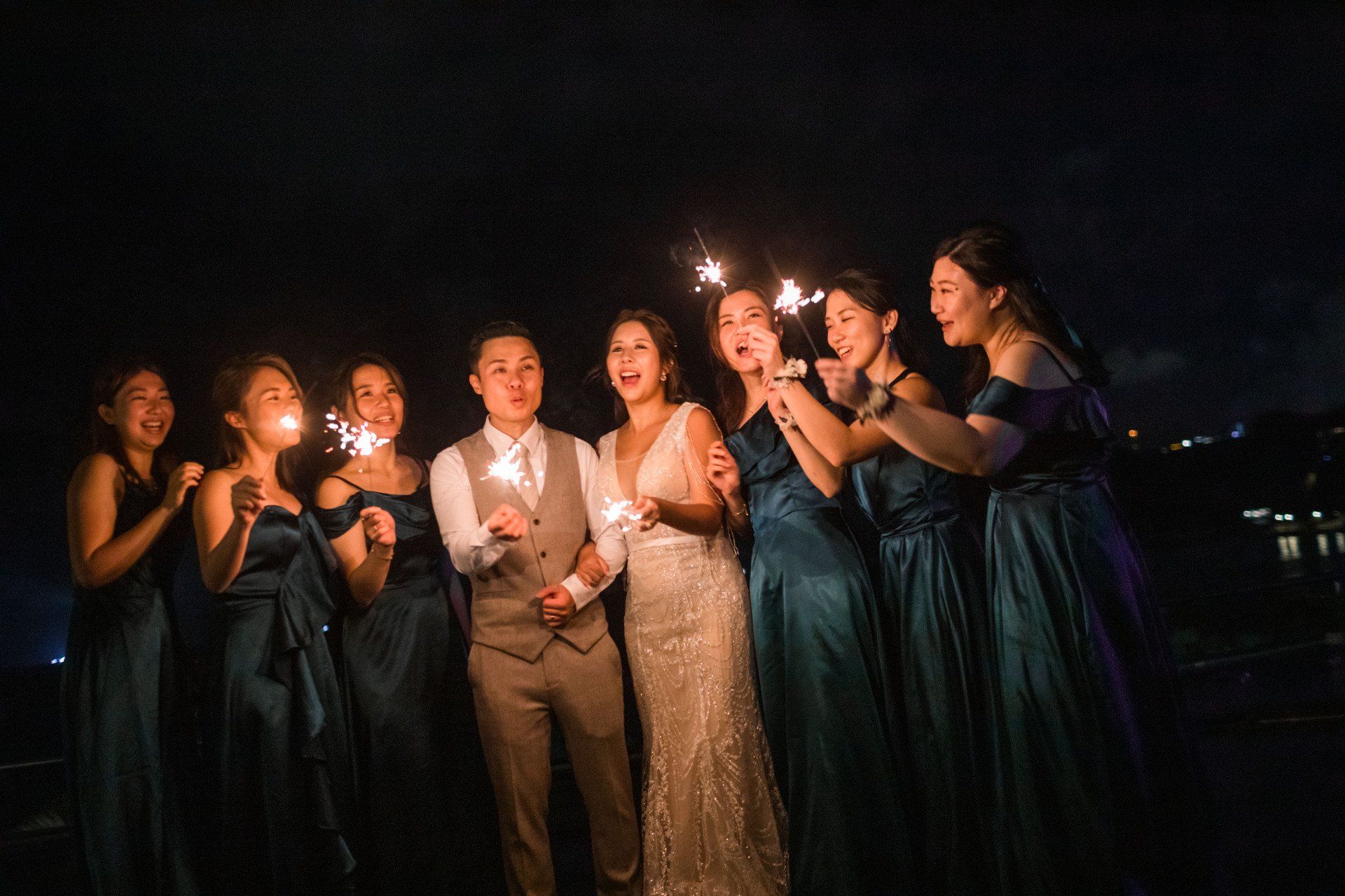 Wedding party holding sparklers at night, with the bride and groom in the center.