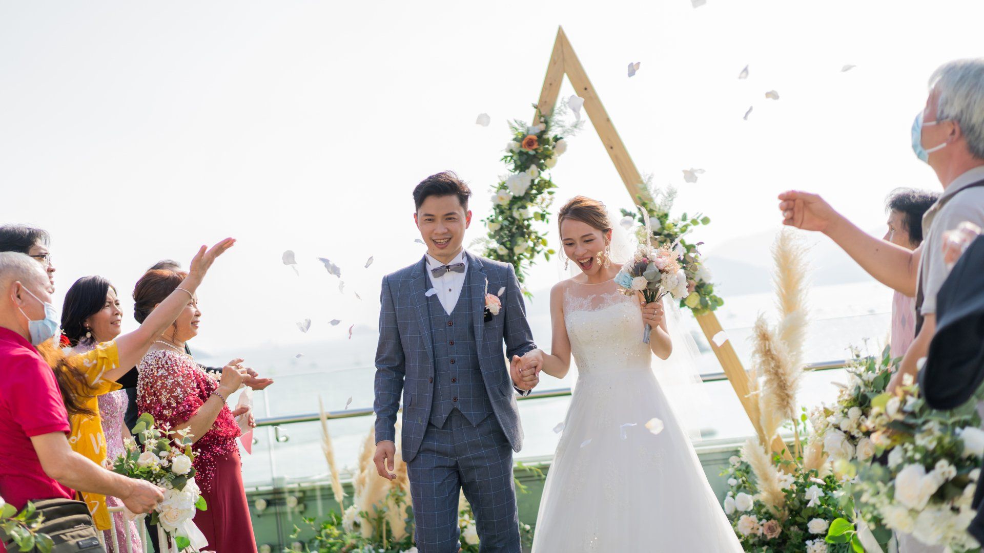 Newlyweds walking under petal shower after wedding ceremony on outdoor terrace.
