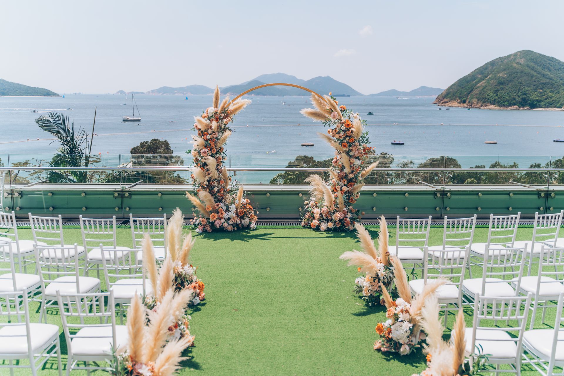 Wedding ceremony setup with arch decorated with flowers and pampas grass, overlooking the ocean.