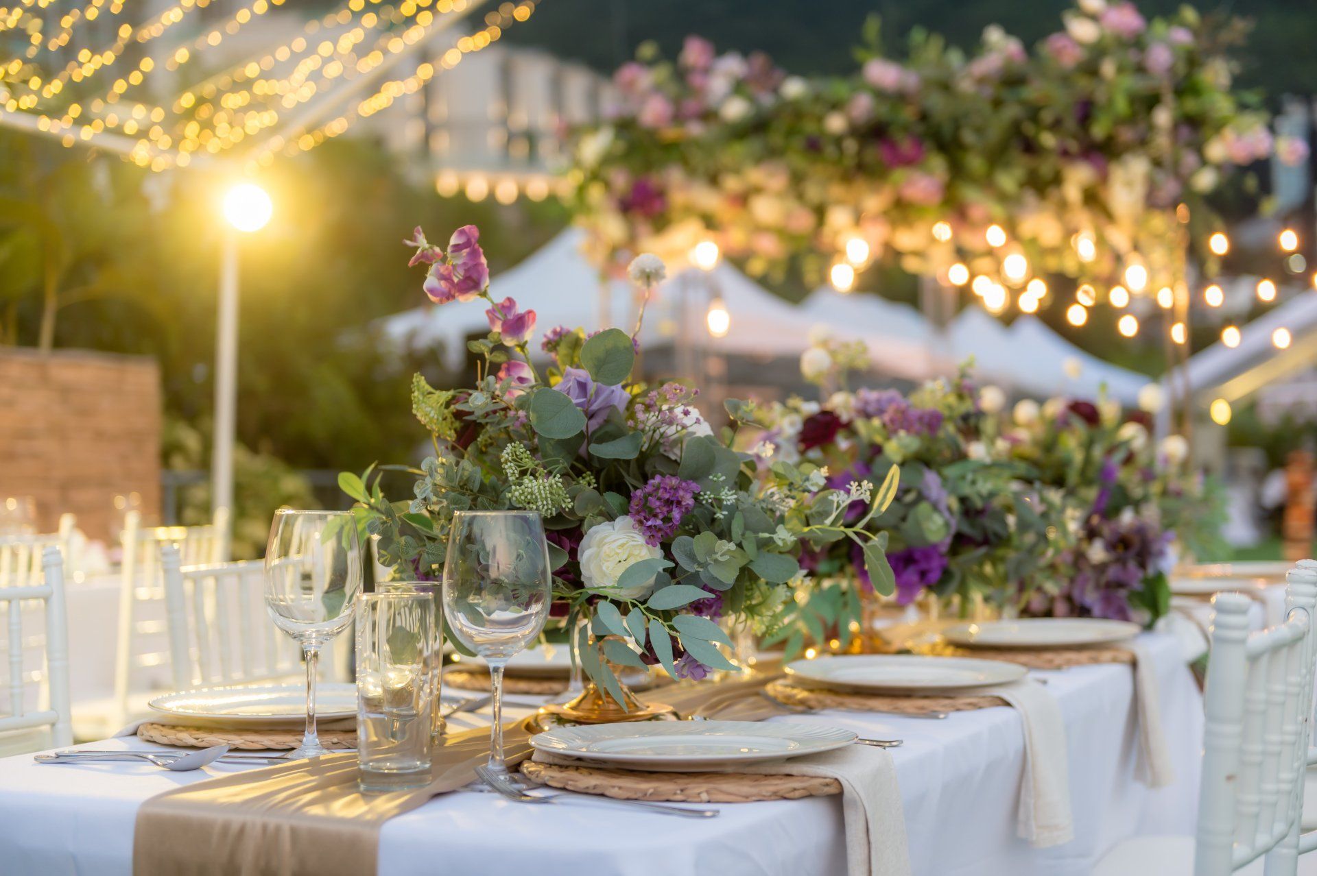 Wedding table set outdoors, decorated with flowers, string lights.