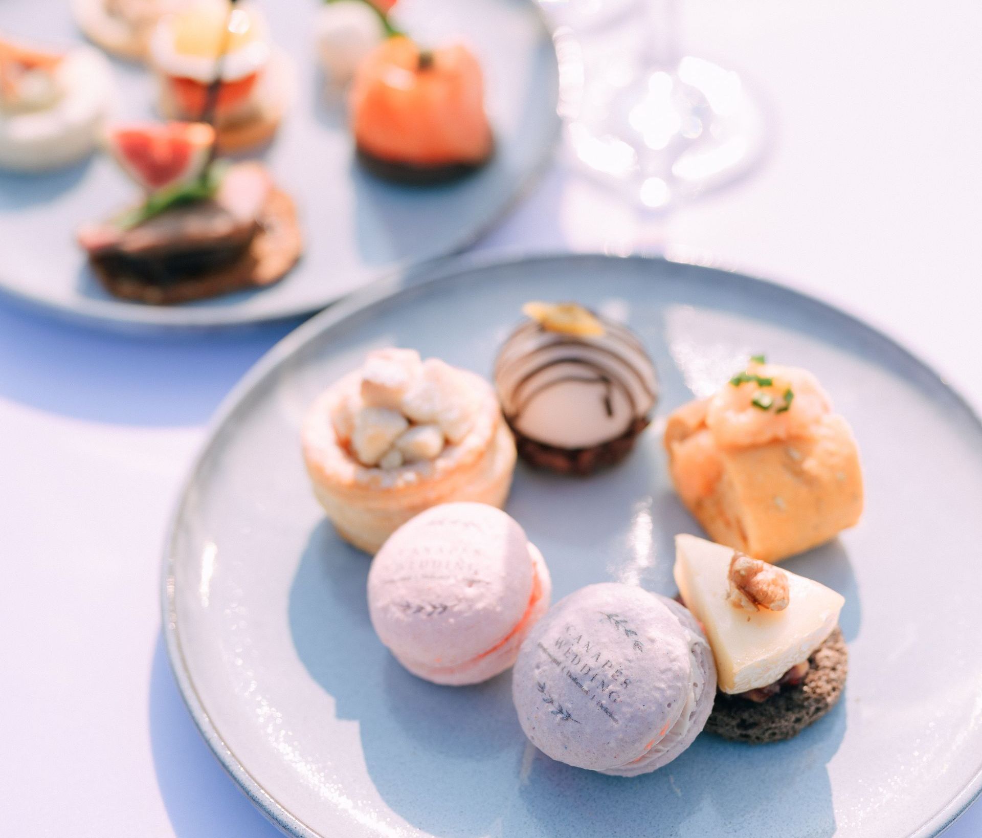 Two light blue plates with assorted appetizers and desserts on a white surface.