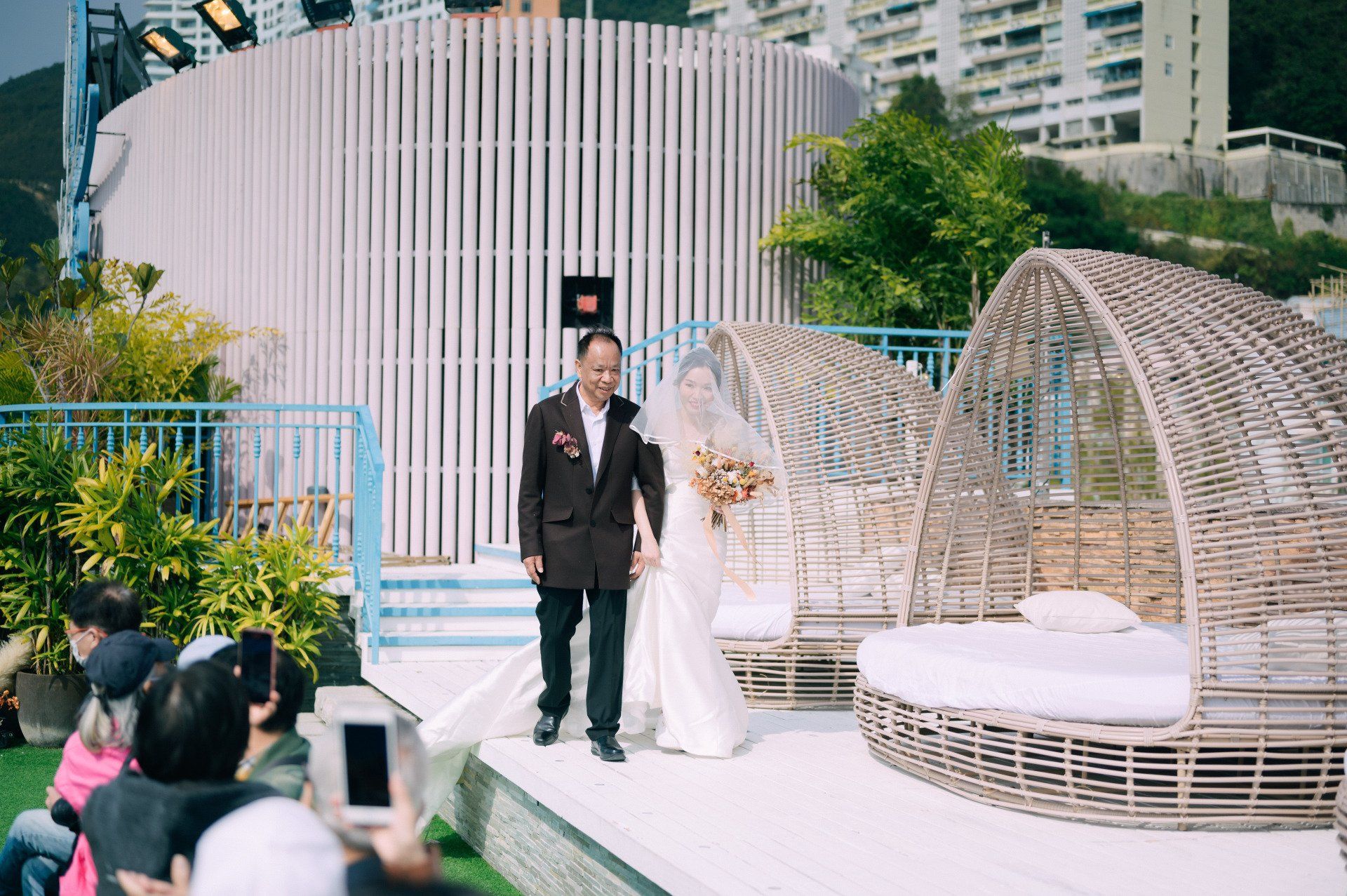 Bride in white dress walks aisle with man in suit at outdoor wedding.