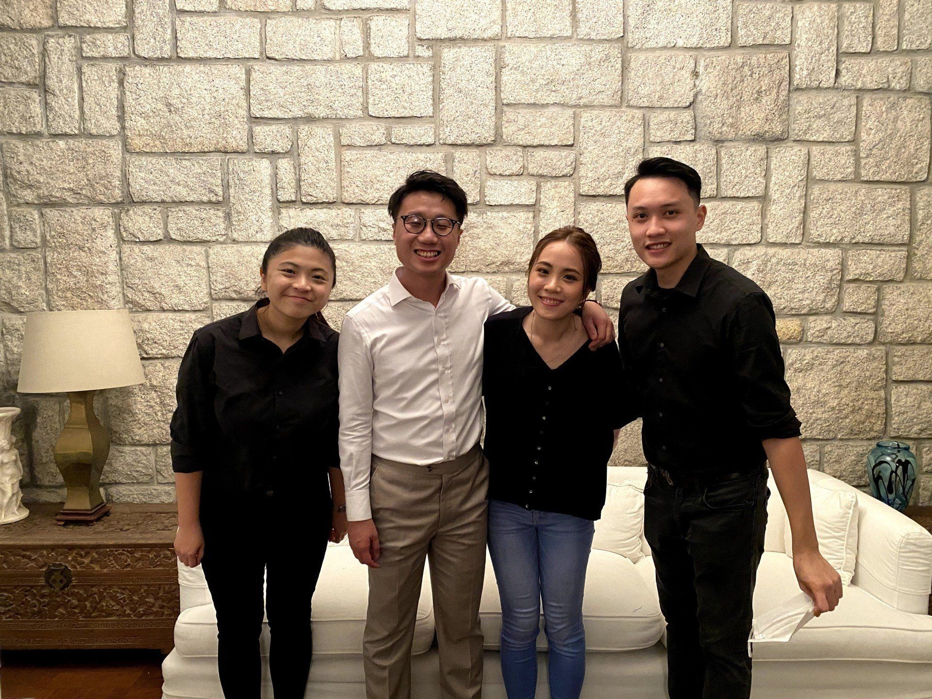 Four people standing in front of a stone wall. Two women and two men, smiling.