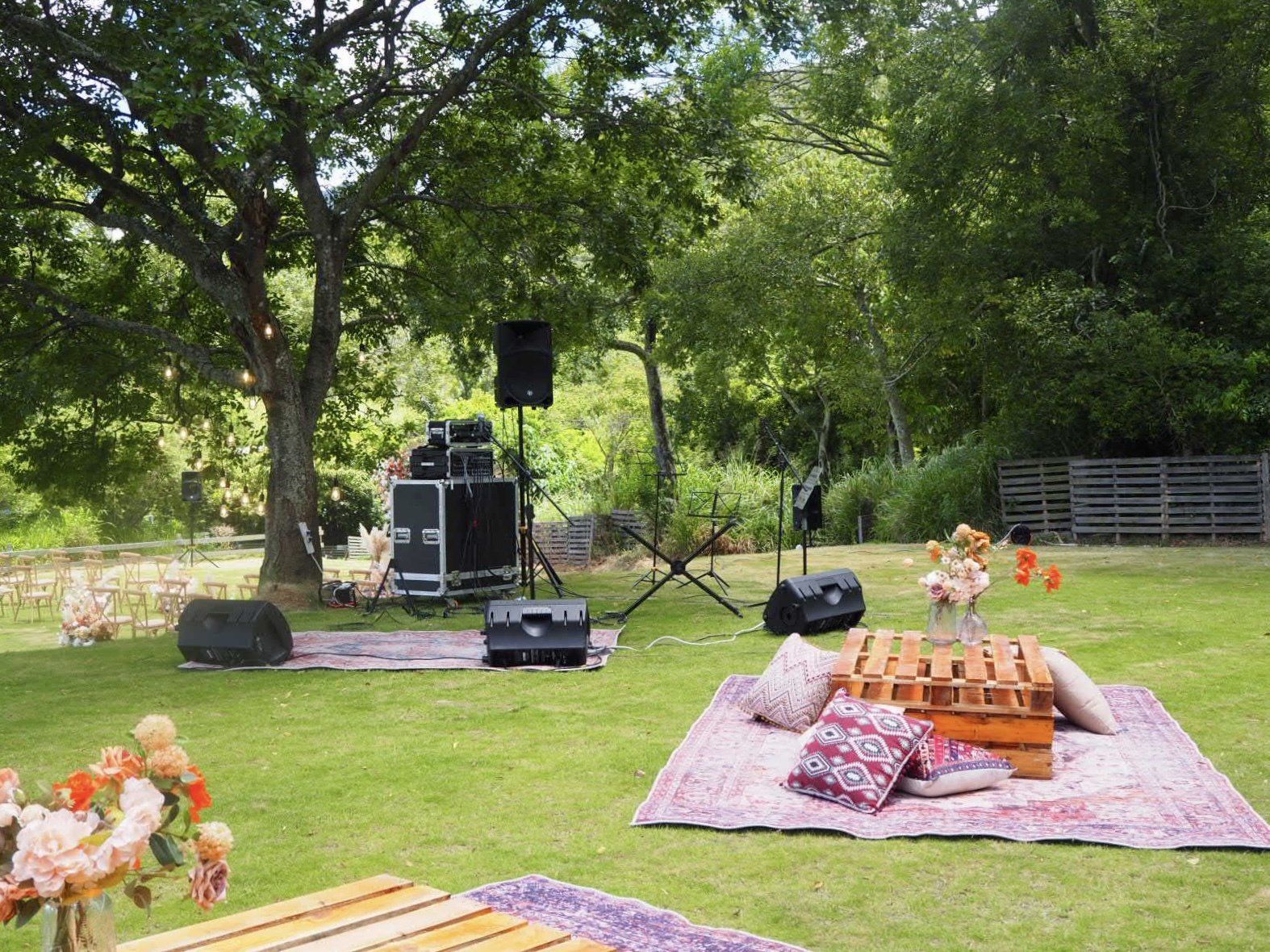 Outdoor event setup with speakers, stage, and seating area on a lawn.