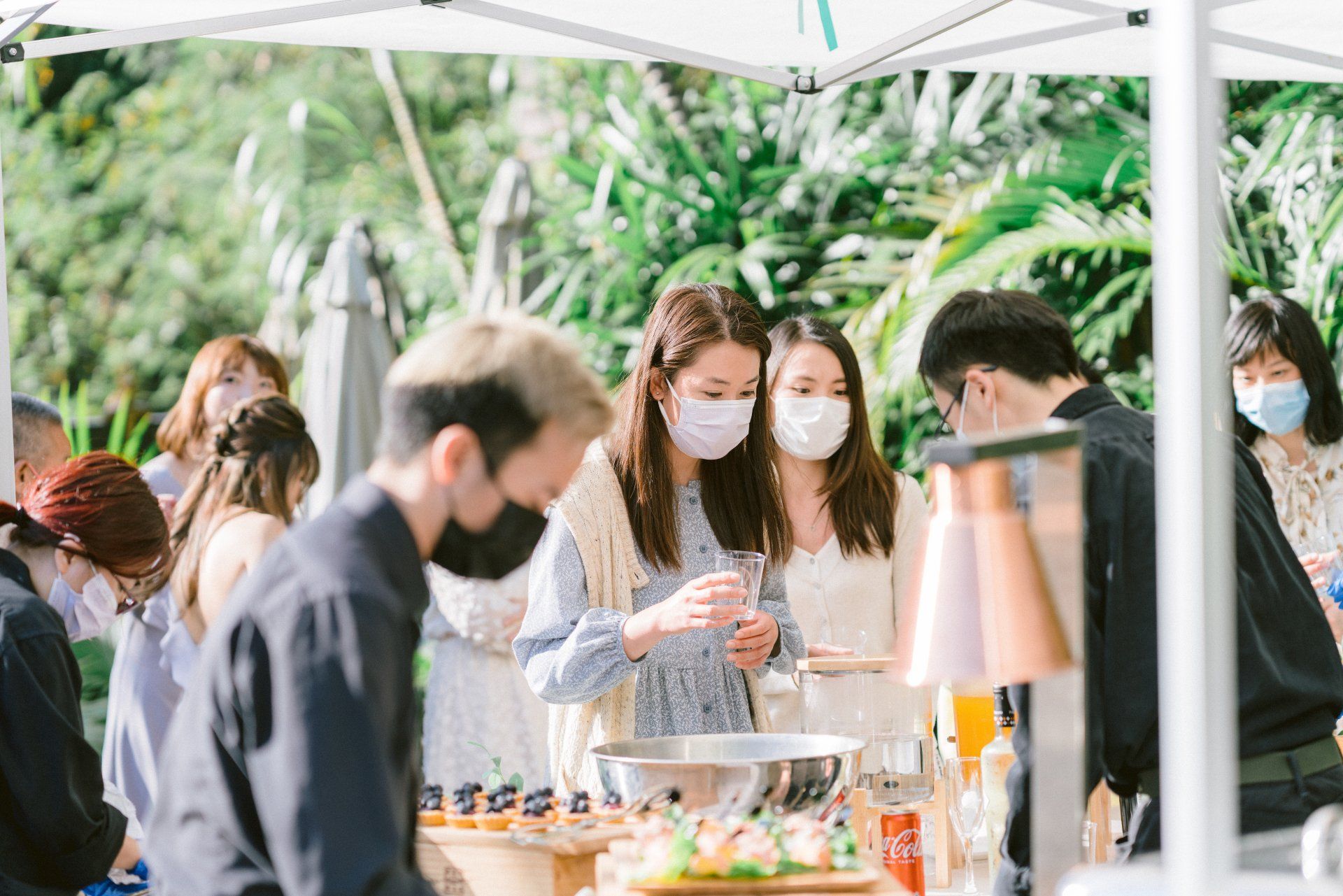 People wearing masks at an outdoor buffet, serving themselves food under a tent.
