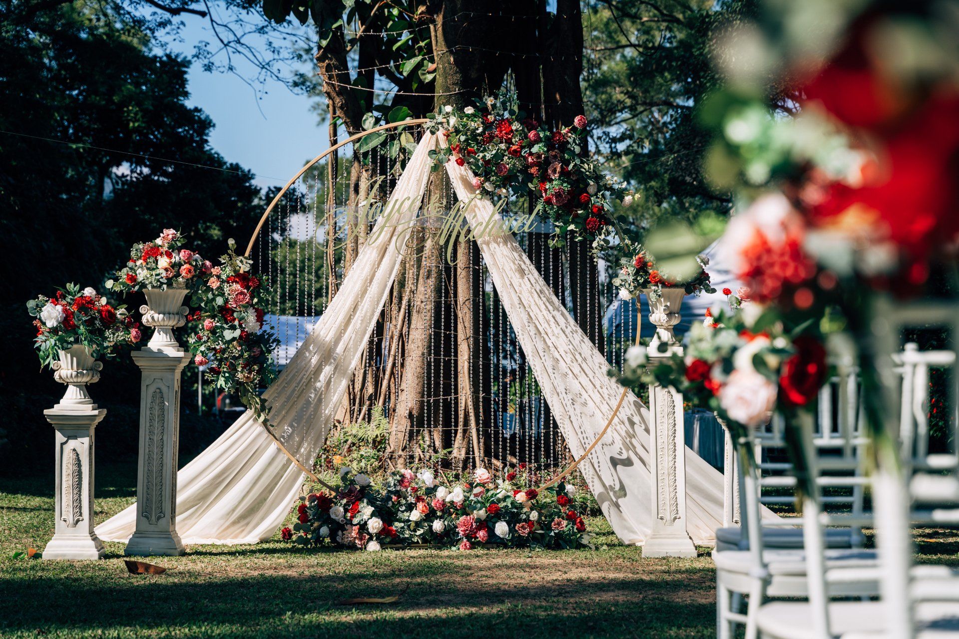 Wedding ceremony setup outdoors with floral arrangements in red, cream, and white.