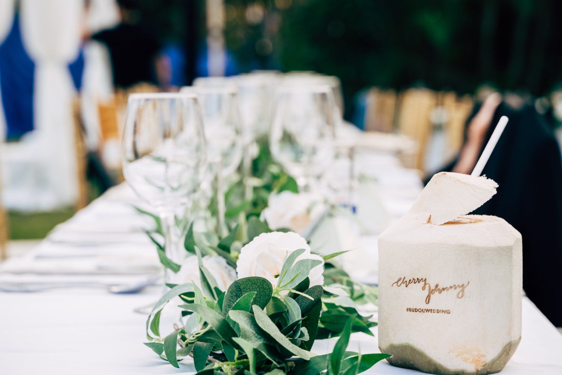 Wedding reception table with coconut drink, greenery, and glassware.