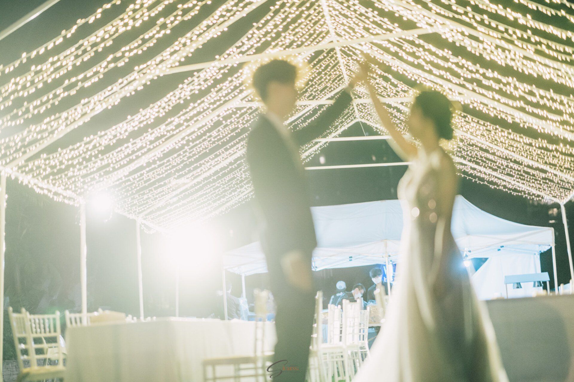 Couple dances under string lights at an outdoor celebration.