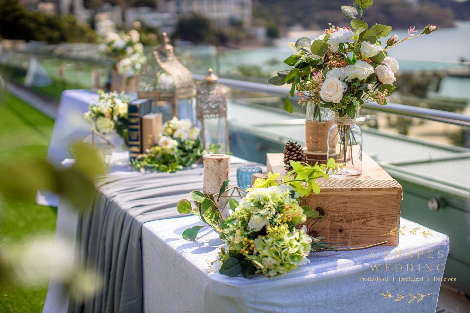 Outdoor table decorated with flowers, books, and candles, overlooking a body of water.