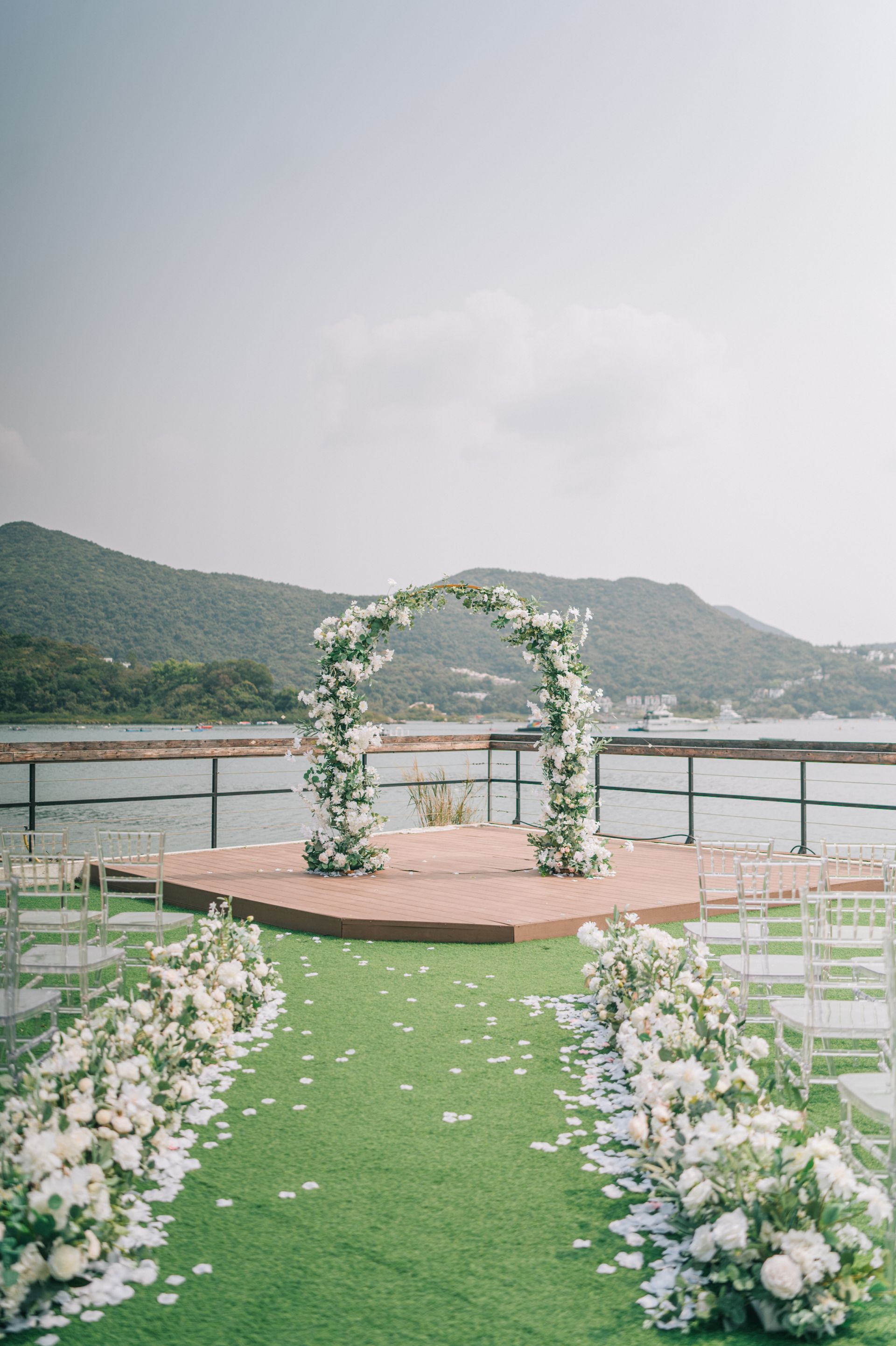 Wedding arch decorated with white flowers on a wooden platform overlooking water.