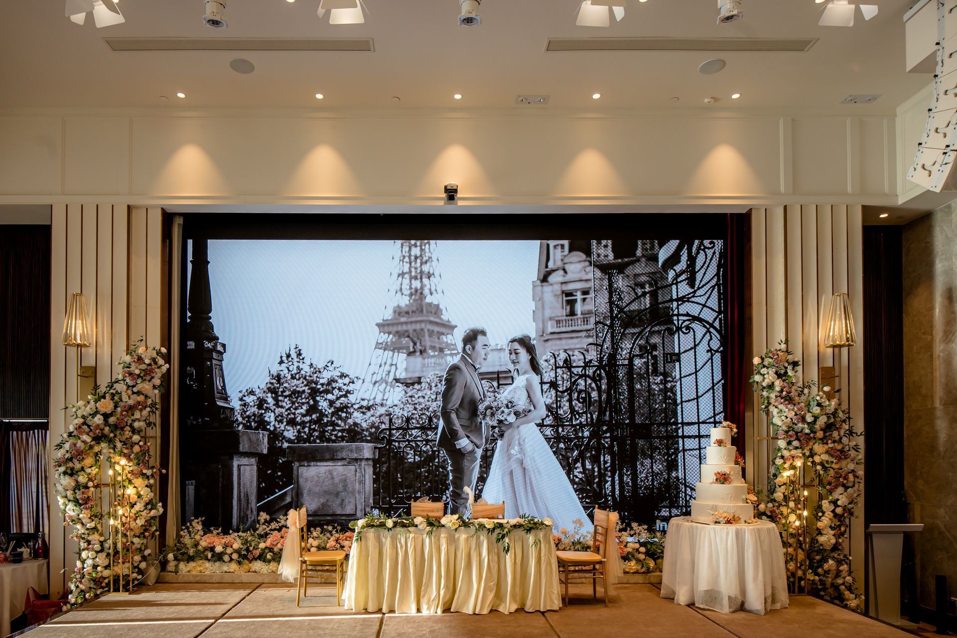 Wedding reception setup with a couple's photo displayed, adorned with floral arrangements and cake.