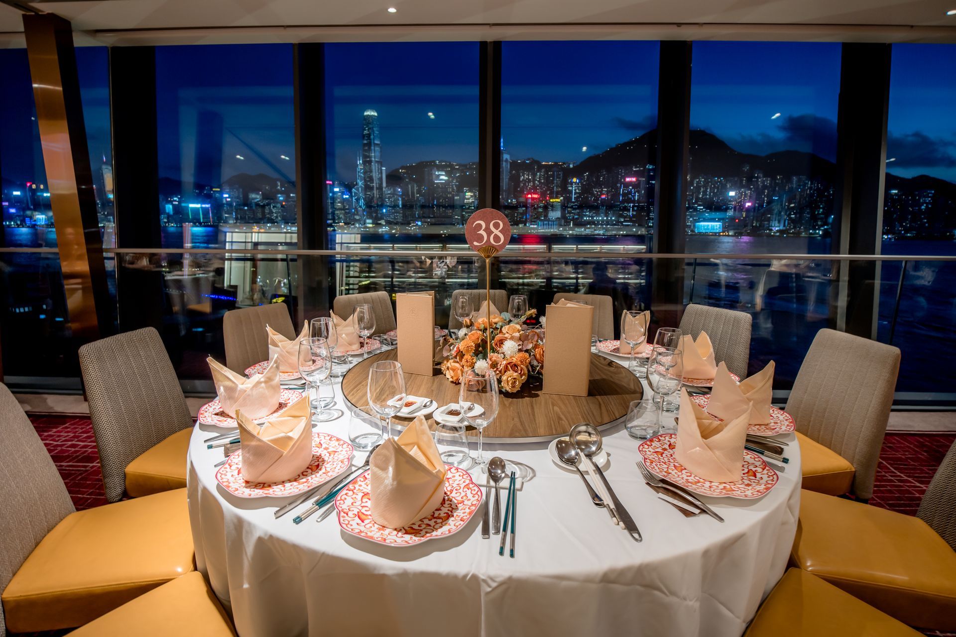 Round dining table set for a formal dinner with a city view at night.