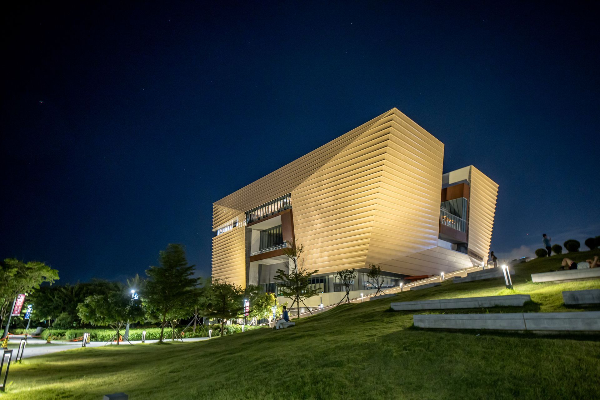 Modern building at night with a honeycomb facade, set on a grassy hill under a dark blue sky.