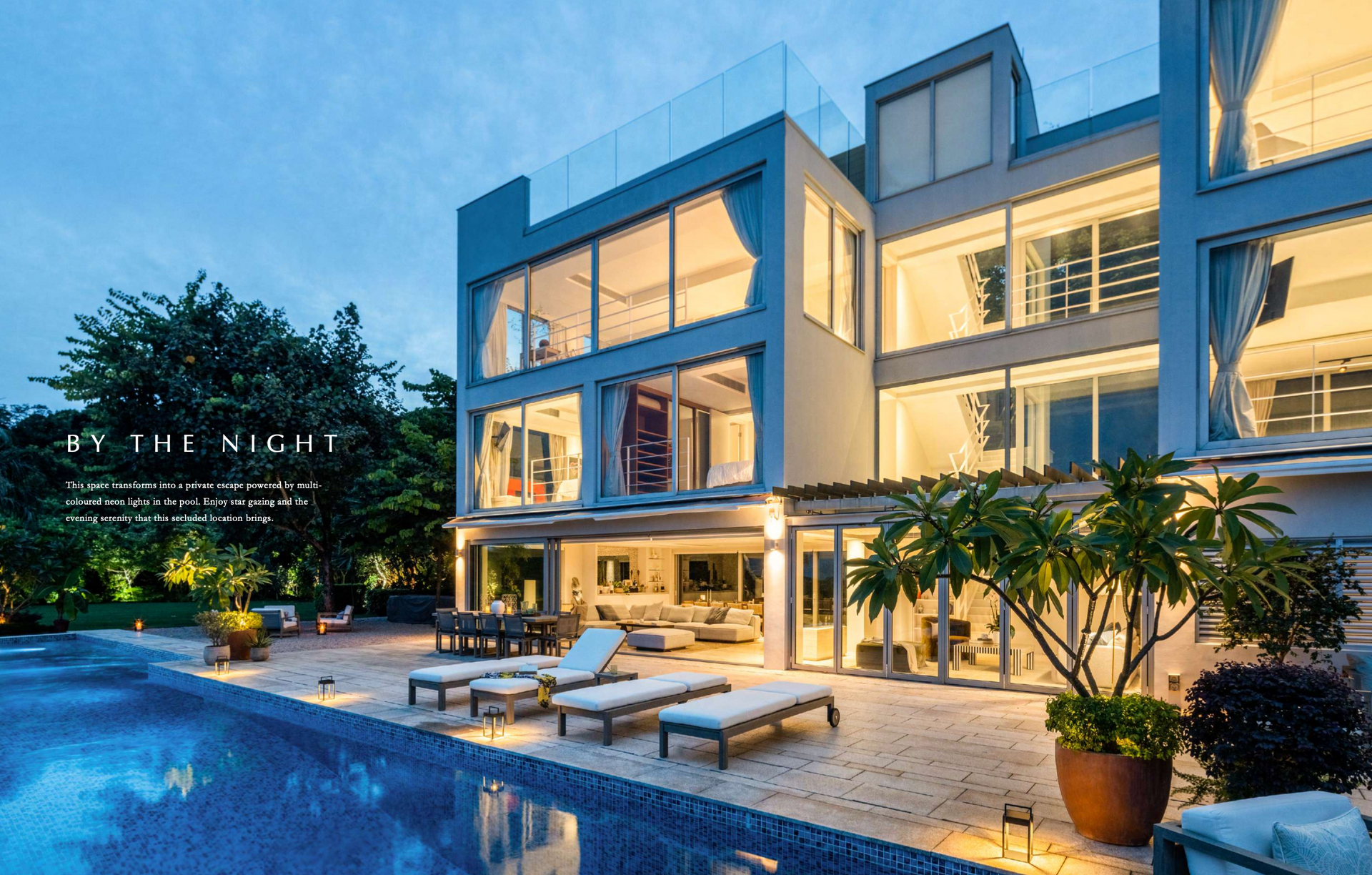 Modern multi-story house with illuminated windows and a pool at dusk.