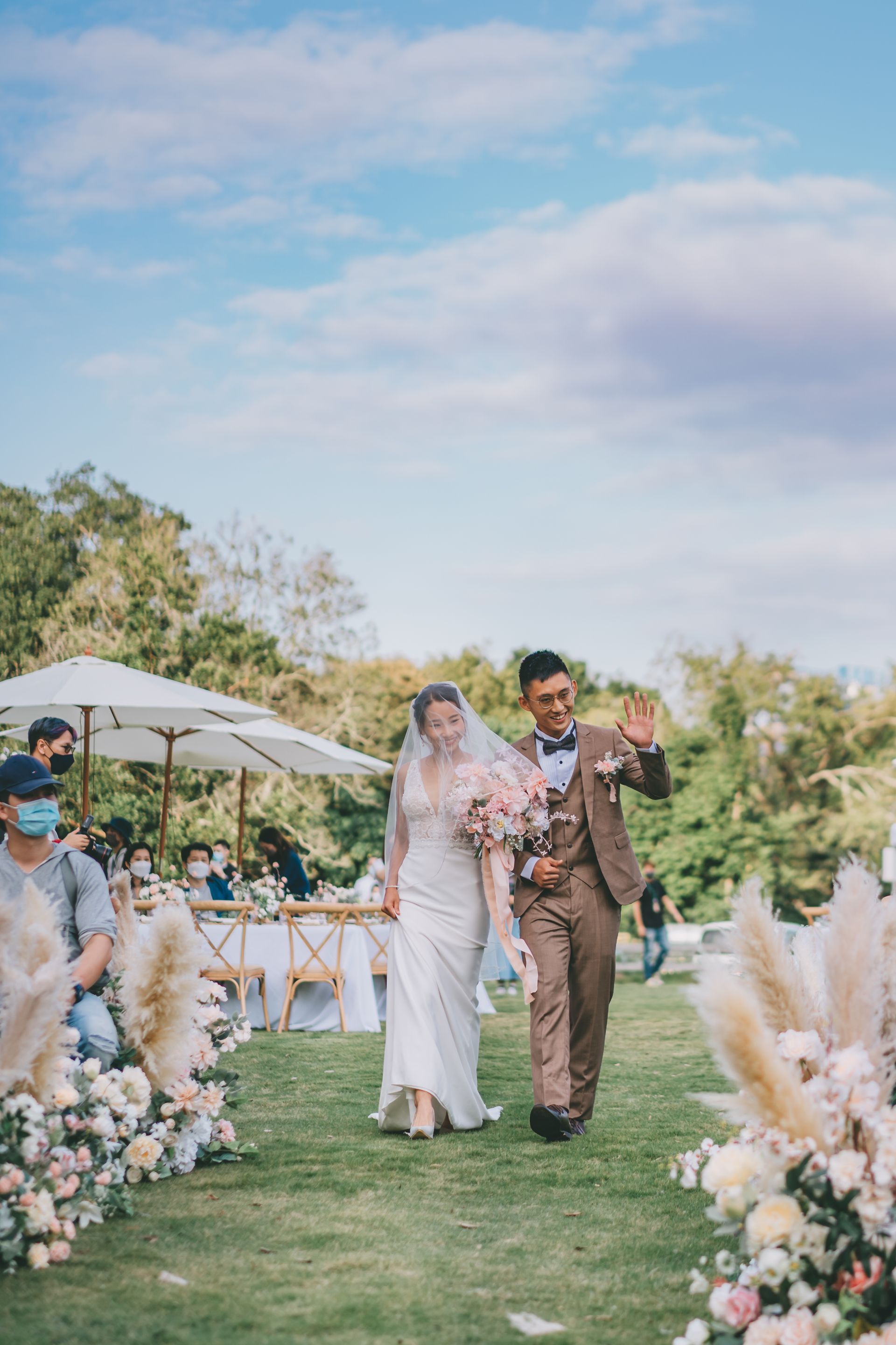 Bride throws bouquet surrounded by guests on a sunny lawn. Ribbons hang from above.