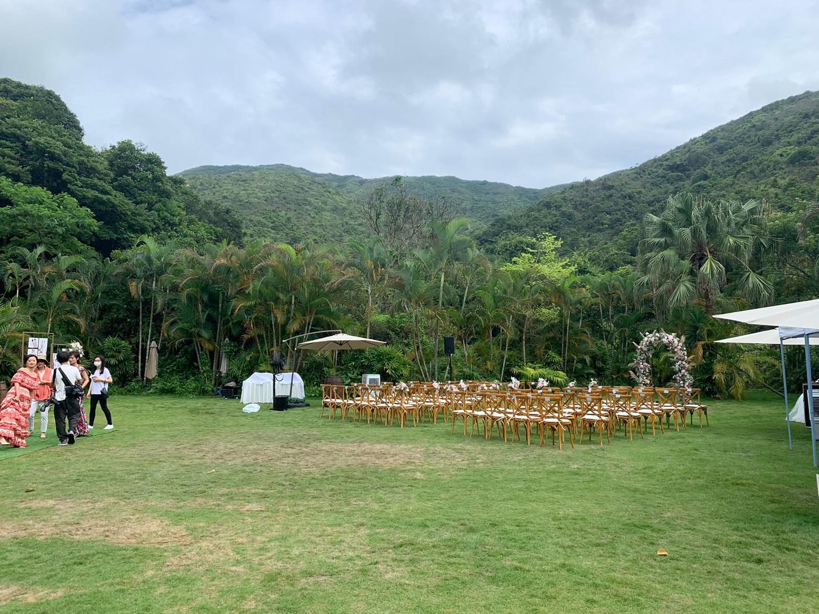 Outdoor wedding setup on a green lawn with chairs, an arch, and mountain backdrop.